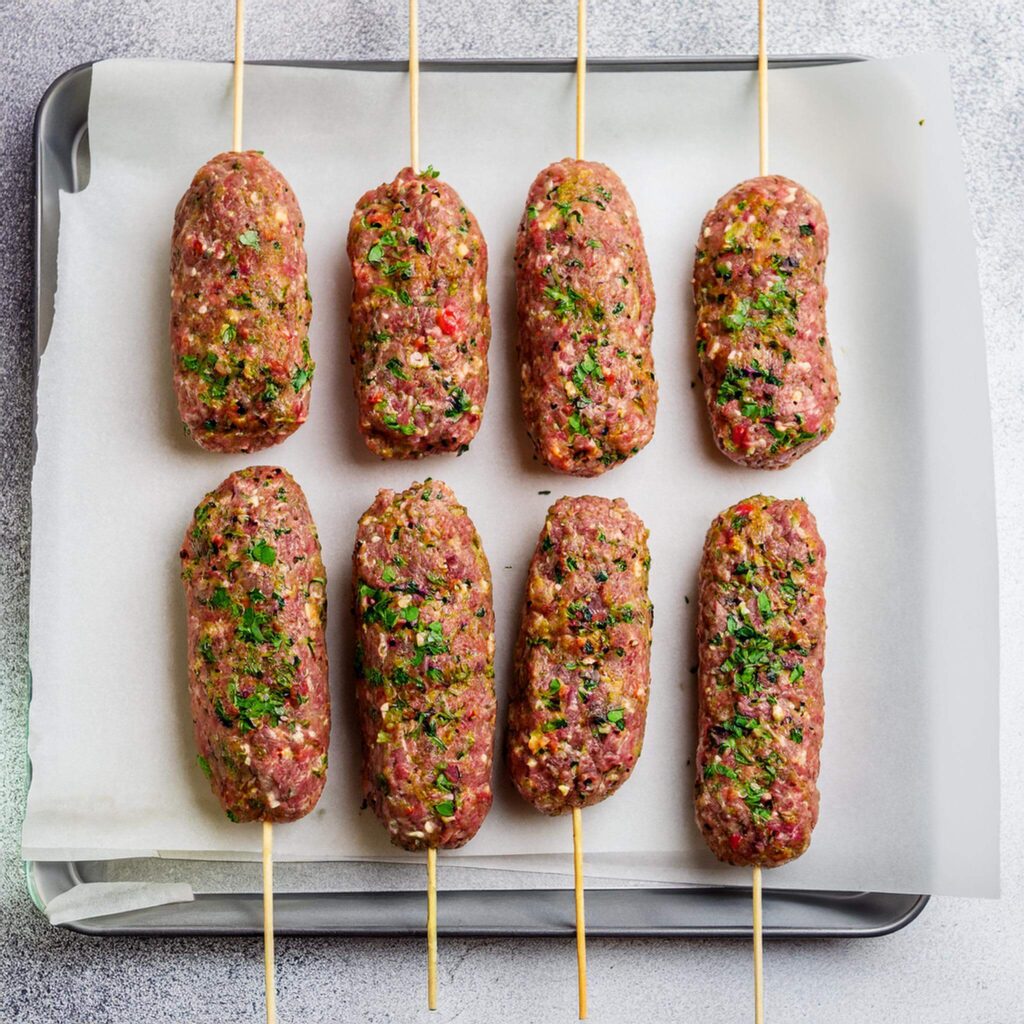 Raw lamb kofta skewers on a parchment-lined baking sheet.