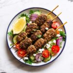 Raw lamb kofta skewers on a parchment-lined baking sheet.