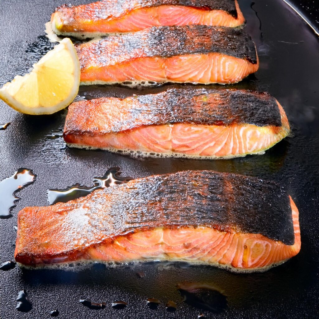 Crispy-skinned salmon fillets with grilled lemon on a skillet.